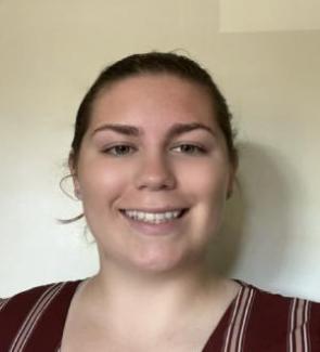 Carrollyn Aasen with brown hair is smiling at the camera. They wear a striped maroon top and stand against a neutral background, conveying a friendly tone.
